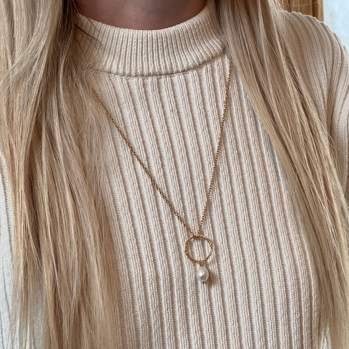 Freshwater pearl pendant, hanging from a gold-plated hammered ring and on a gold-plated chain. Worn by a model with an ivory jumper
