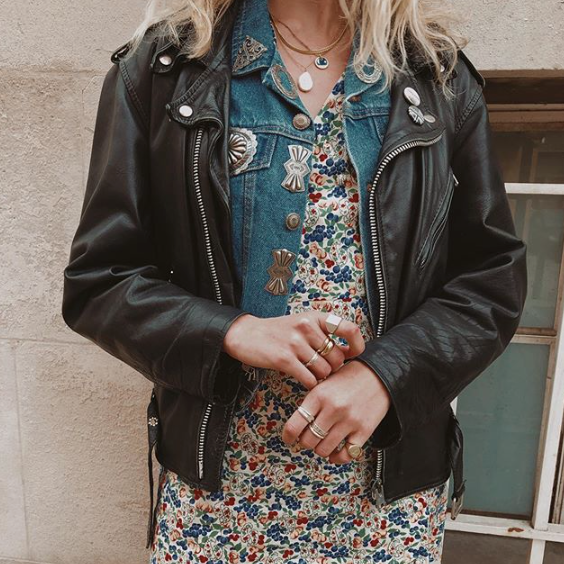 A model wearing a moon and star pendant with another pendant. Outside with a flowered dress and a denim and leather acket,