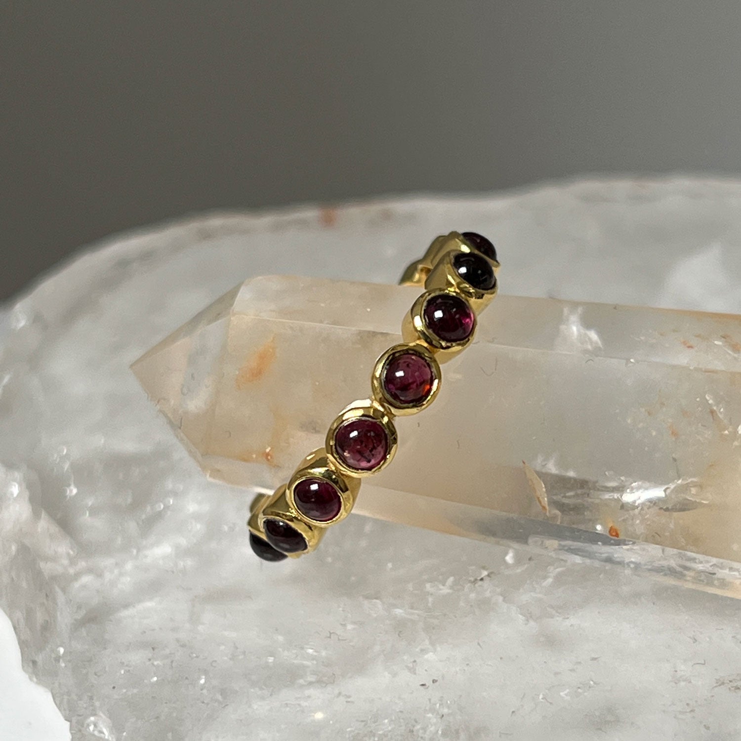 An eternity vermail garnet cabochon ring against a backdrop of crystals