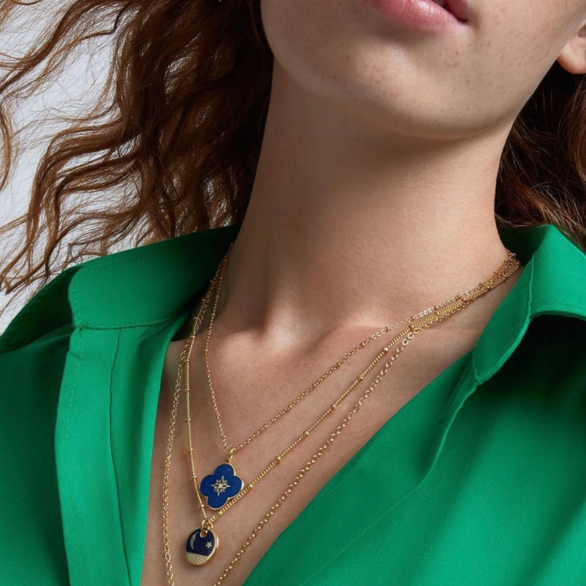 Close-up of a person wearing a gold necklace with a blue pendant against a green shirt.
