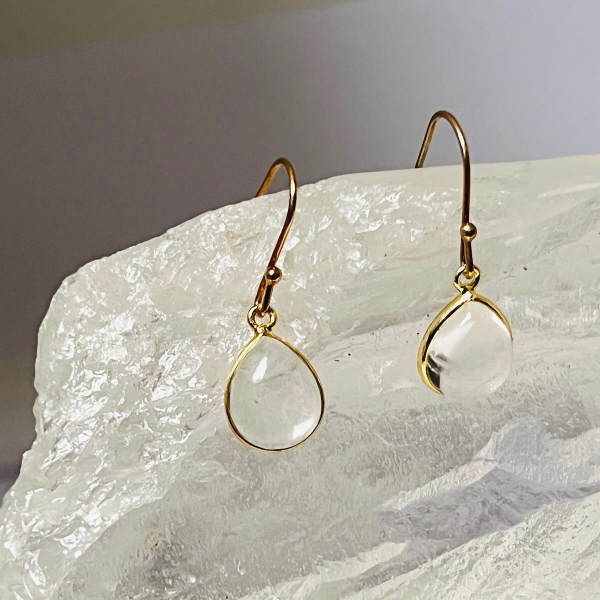 Gold earrings with clear teardrop-shaped stones on a textured white surface
