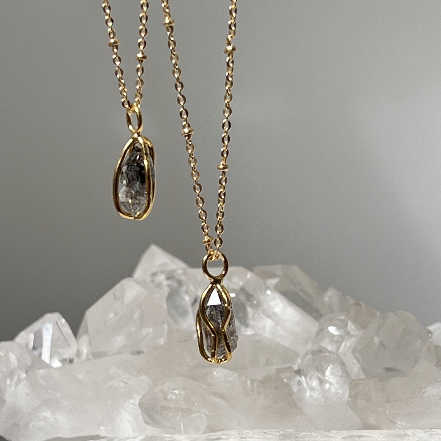 A close up of two Raw Herkimer Quartz Diamond Gold-Plated Cage Pendants with a bed of crystals in the background.