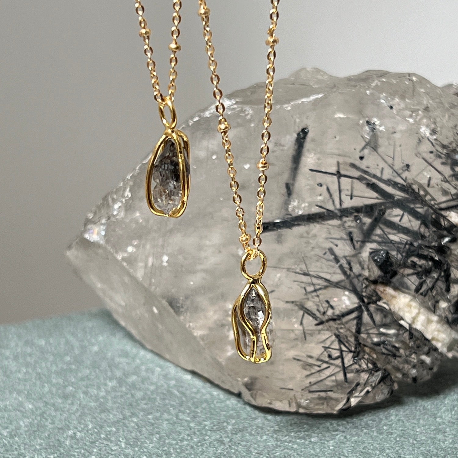 A close up of two Raw Herkimer Quartz Diamond Gold-Plated Cage Pendants with a bed of crystals in the background.
