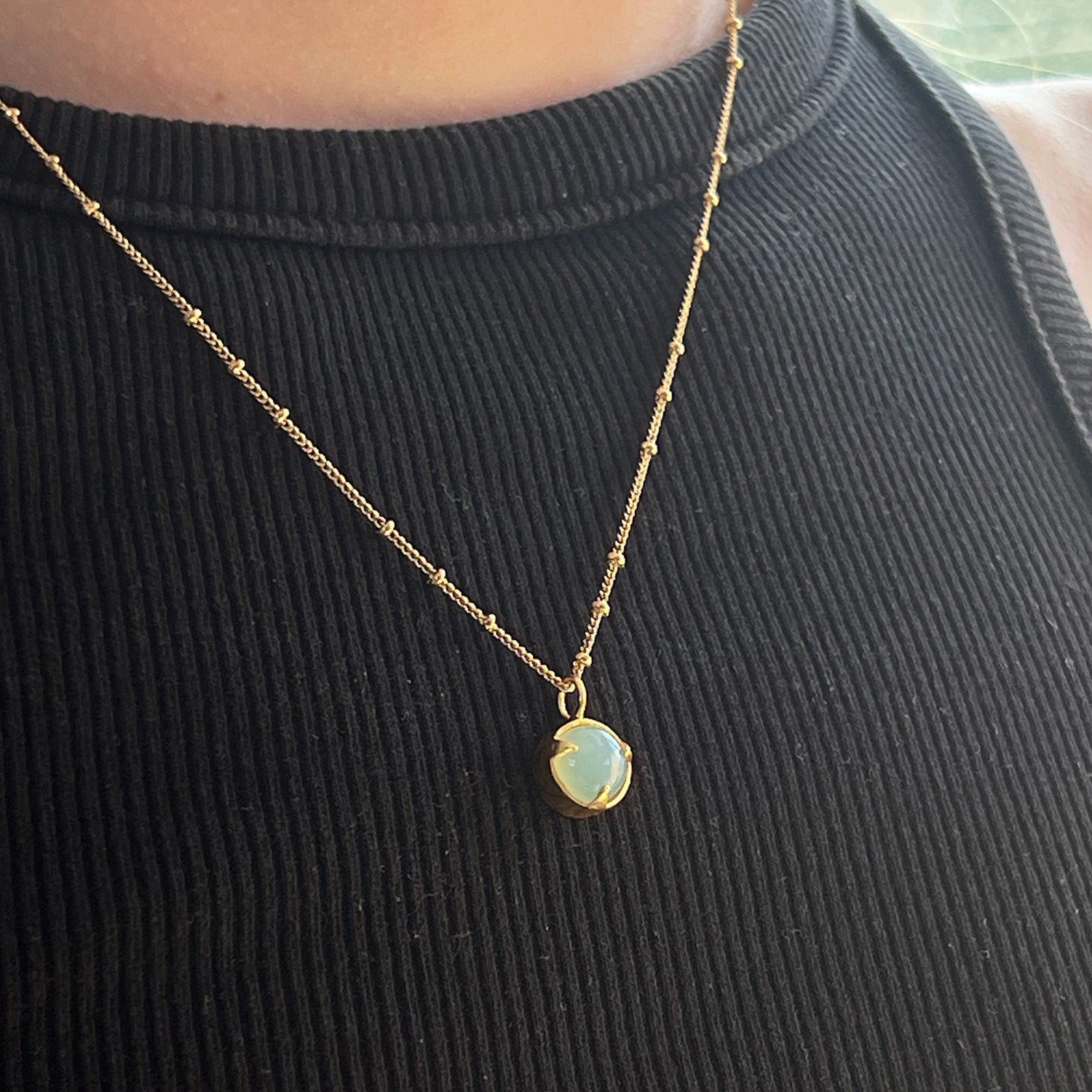Gold necklace with an aqua chalcedony pendant on a black ribbed top