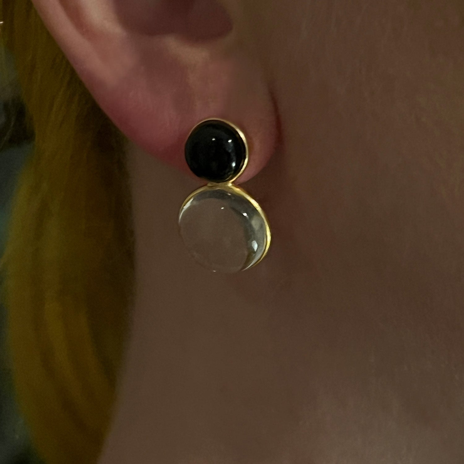 Close-up of an earring with a black gemstone and clear stone on a person's ear.