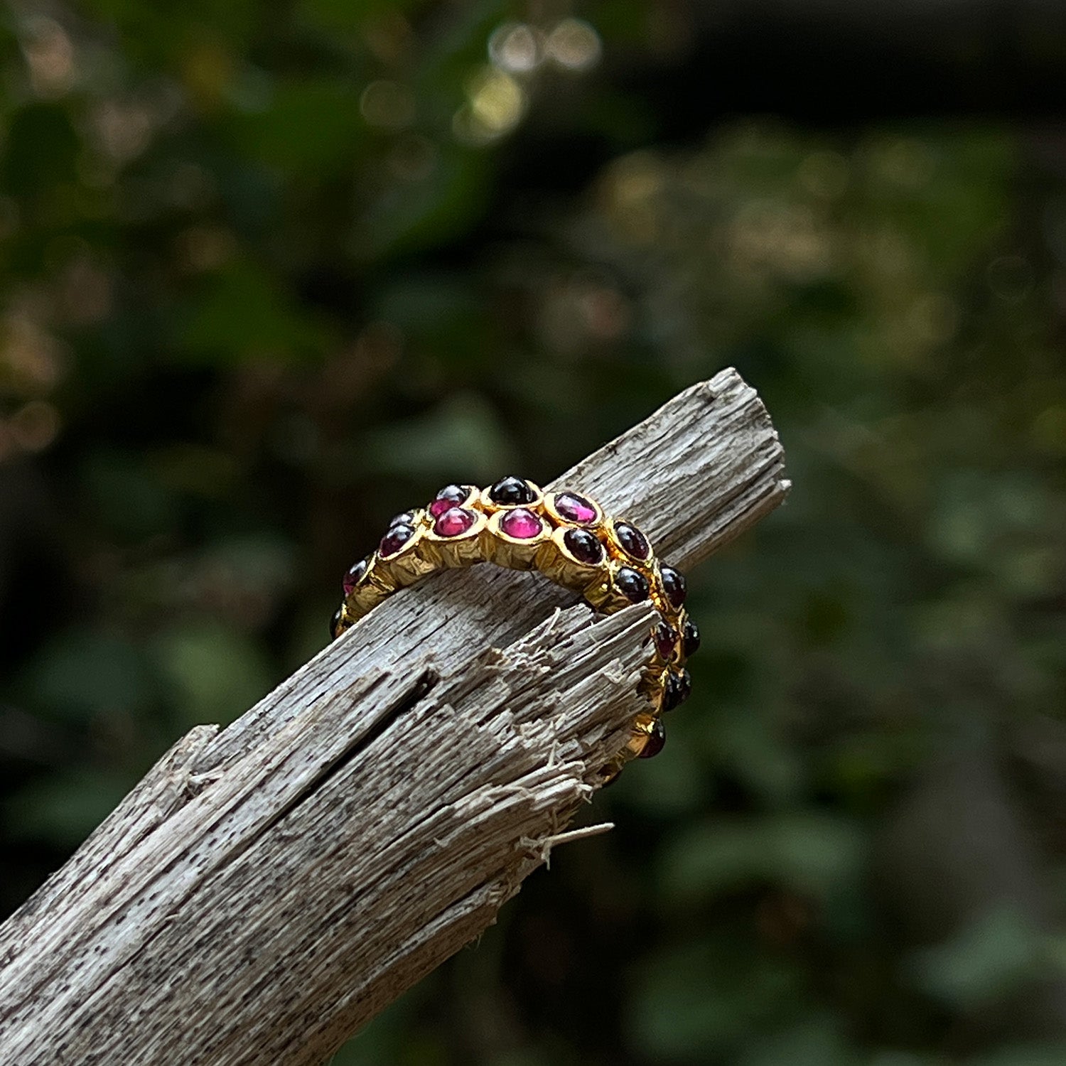 Two gold rings with garnet stones on a wooden branch with a blurred natural background