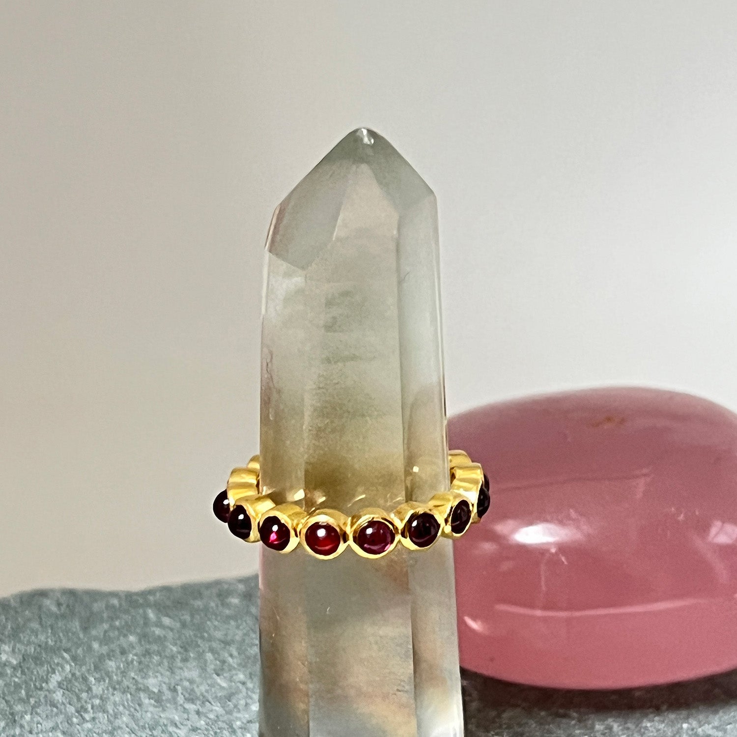 An eternity garnet cabochon ring with gold plating on sterling silver, with multiple crystals in the background