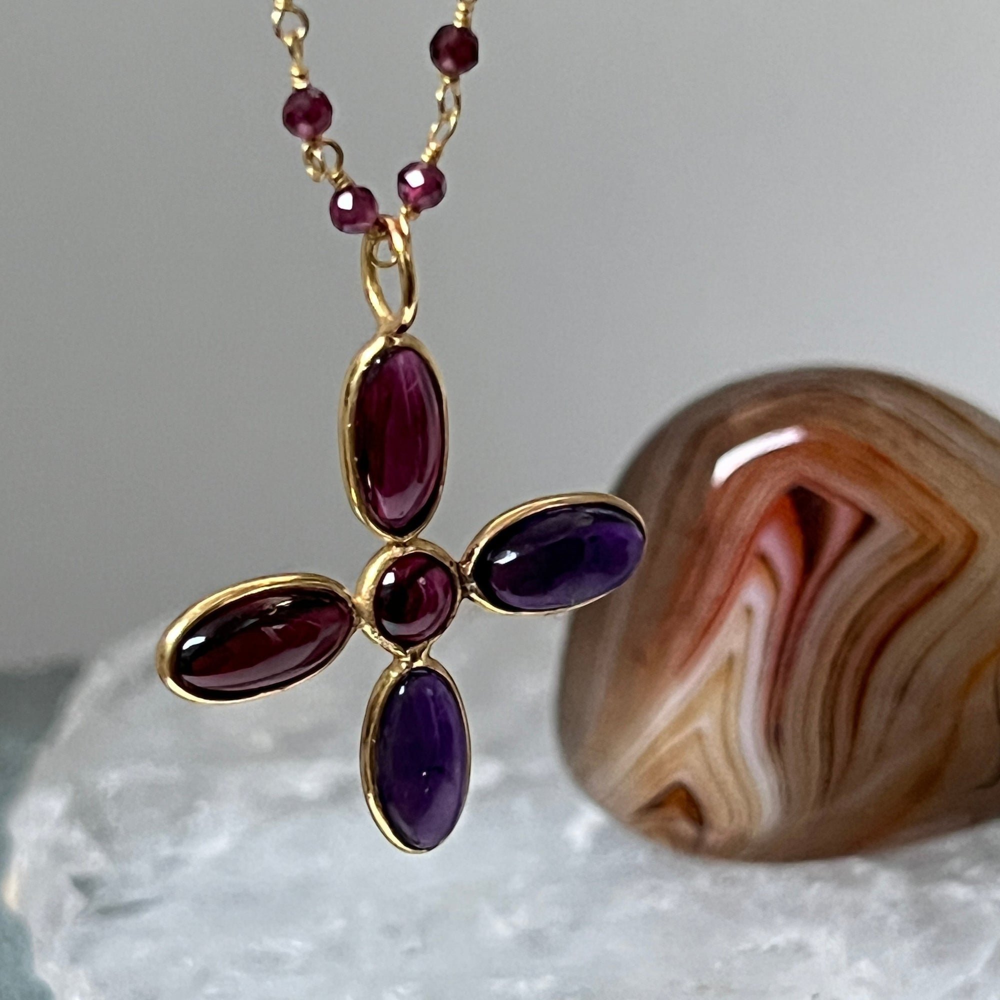 Gold necklace with amethyst and garnet stones on a grey background