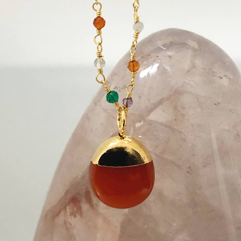 A gold-plated brass rosary necklace with a series of multicolored precious and semi-precious stones and a prominent carnelian pebble at the center. 