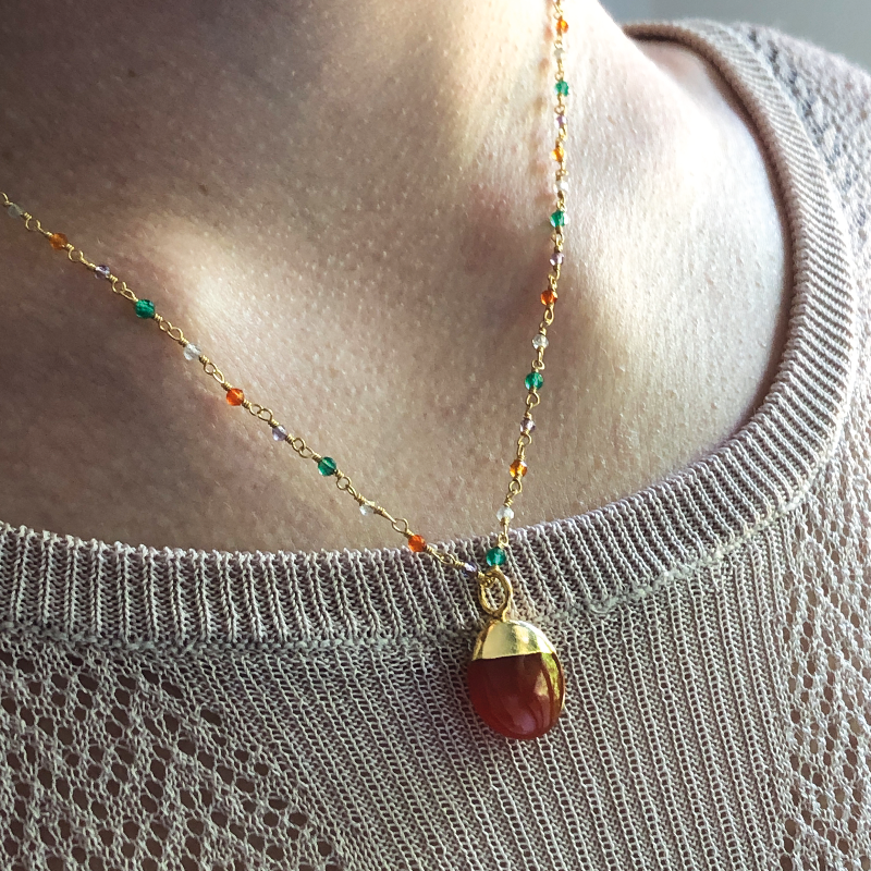 42cm Rosary Necklace with a Carnelian Pebble. 22ct Gold Plated chain with Carnelian, Amethyst, Labradorite, Green Onyx & Garnet. Worn on a camel-coloured jumper.