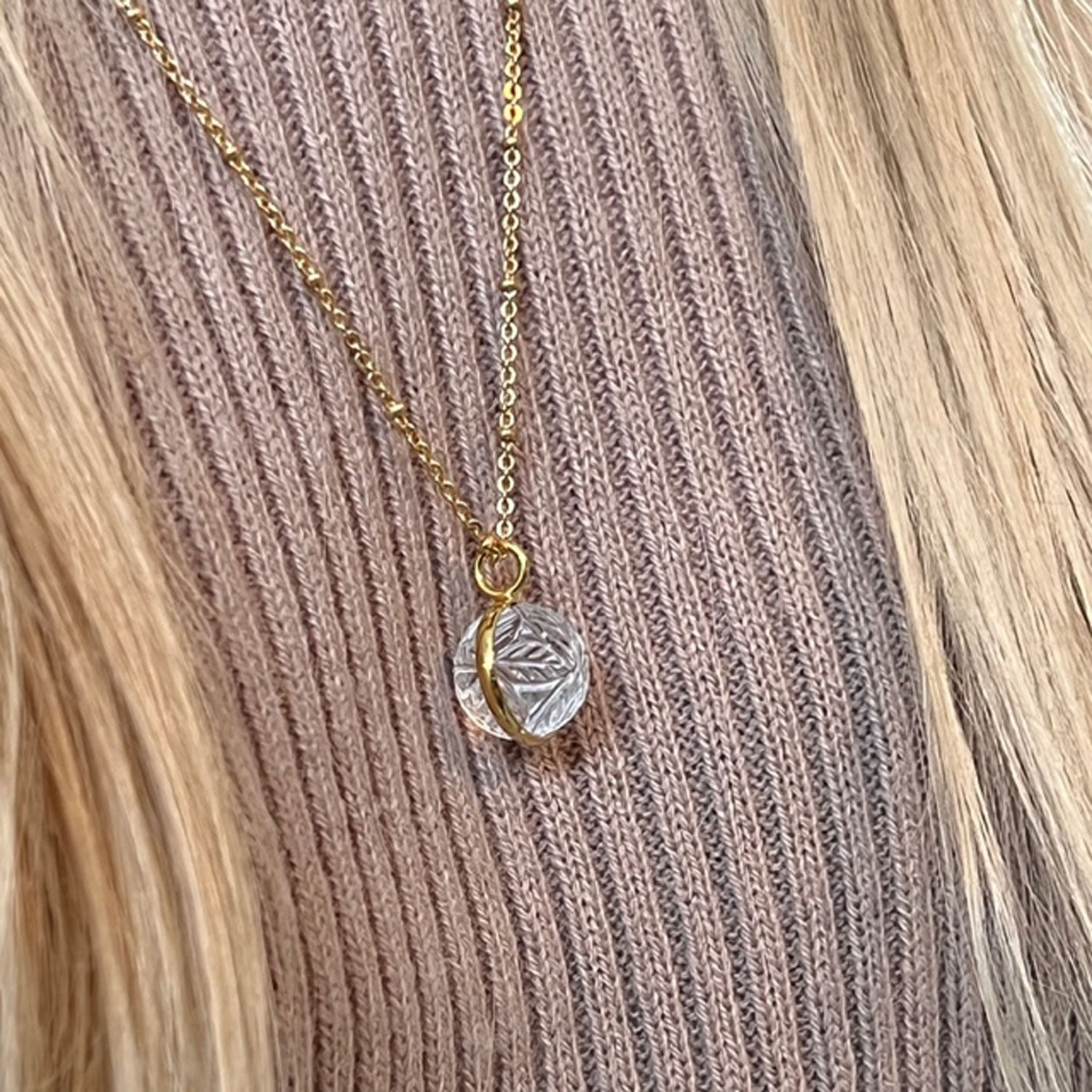Carved rock ball pendant worn on top of a camel jumper