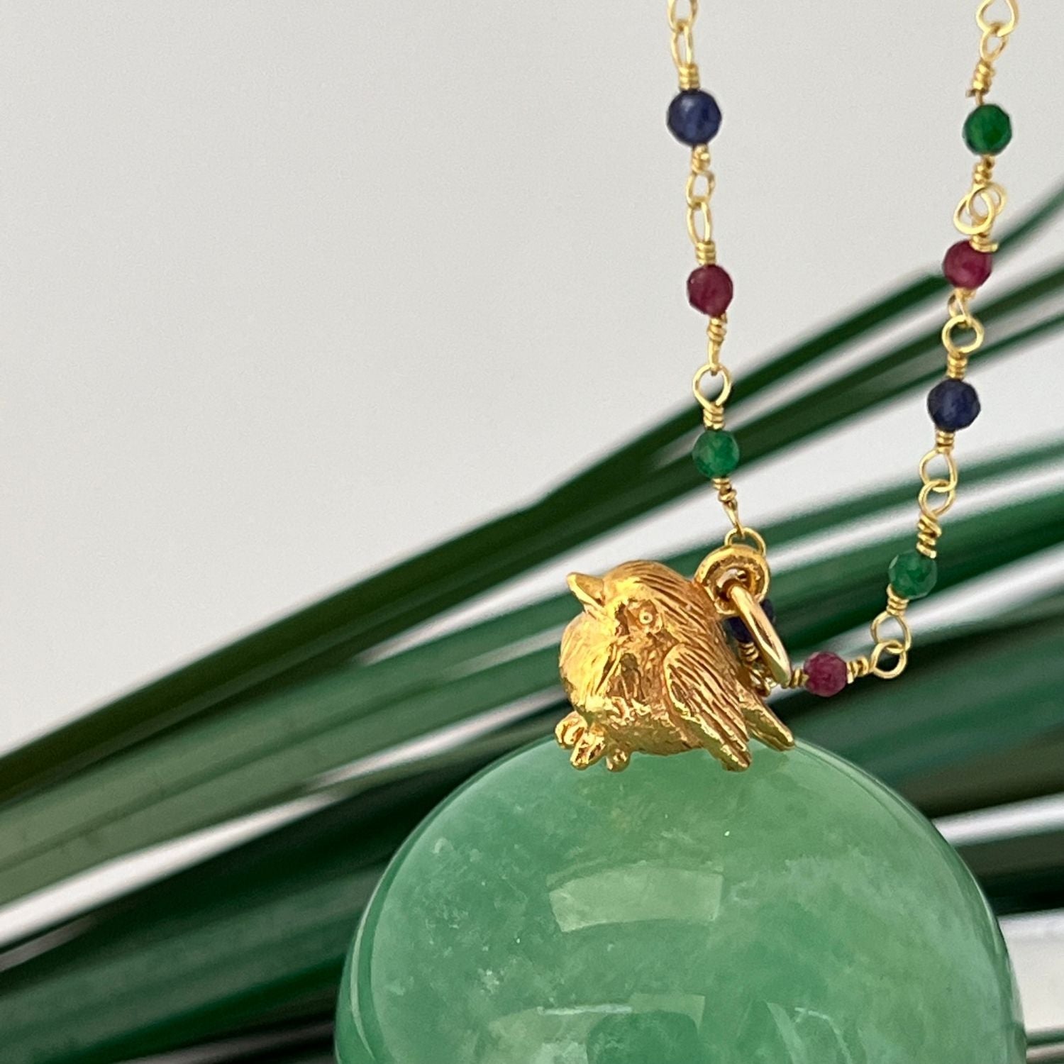 22ct Gold Plated Rosary necklace with Ruby, Saphhire and Emerald. Complete with a Robin charm. Sitting on a green crystal