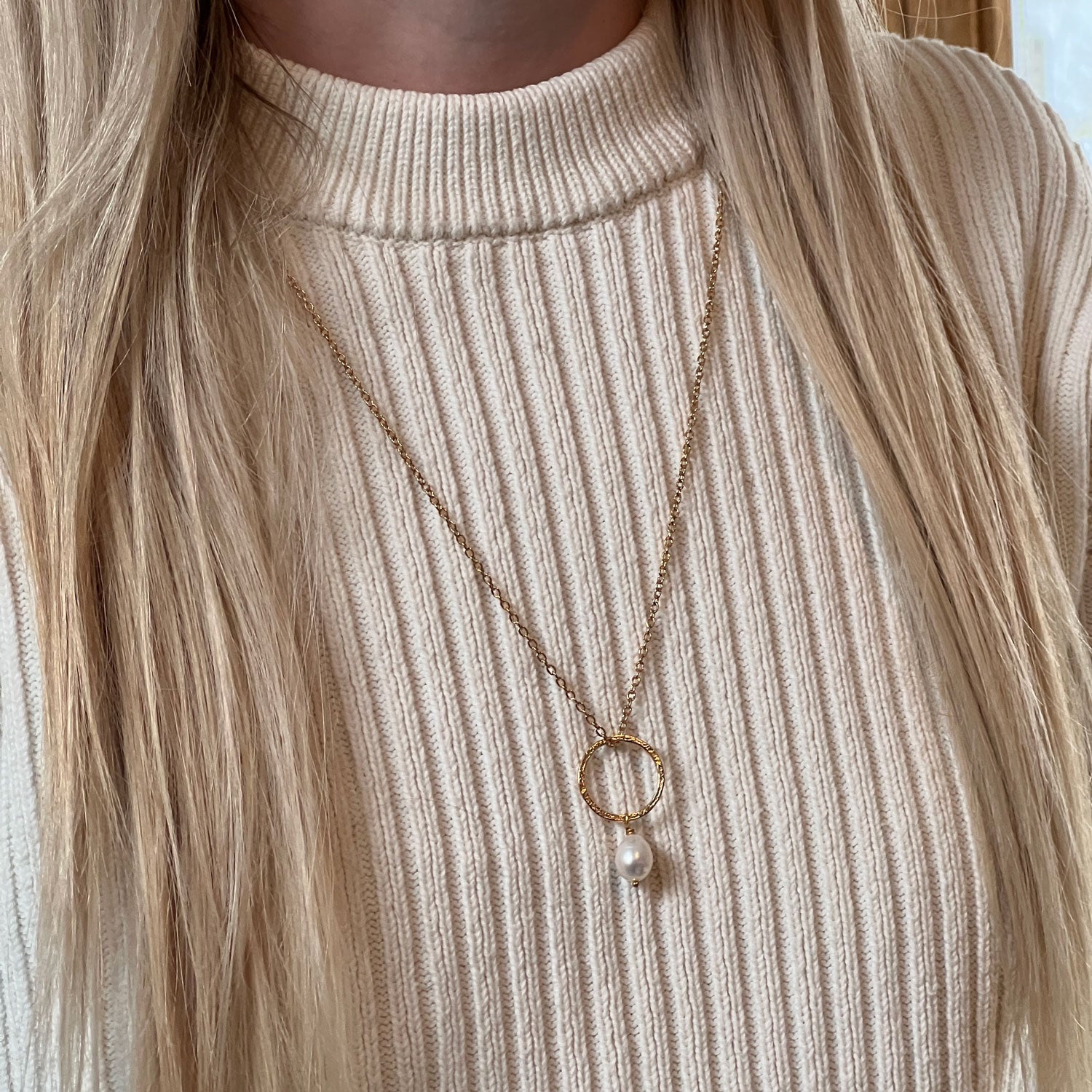 Freshwater pearl pendant, hanging from a gold-plated hammered ring and on a gold-plated chain. Worn by a model with an ivory jumper